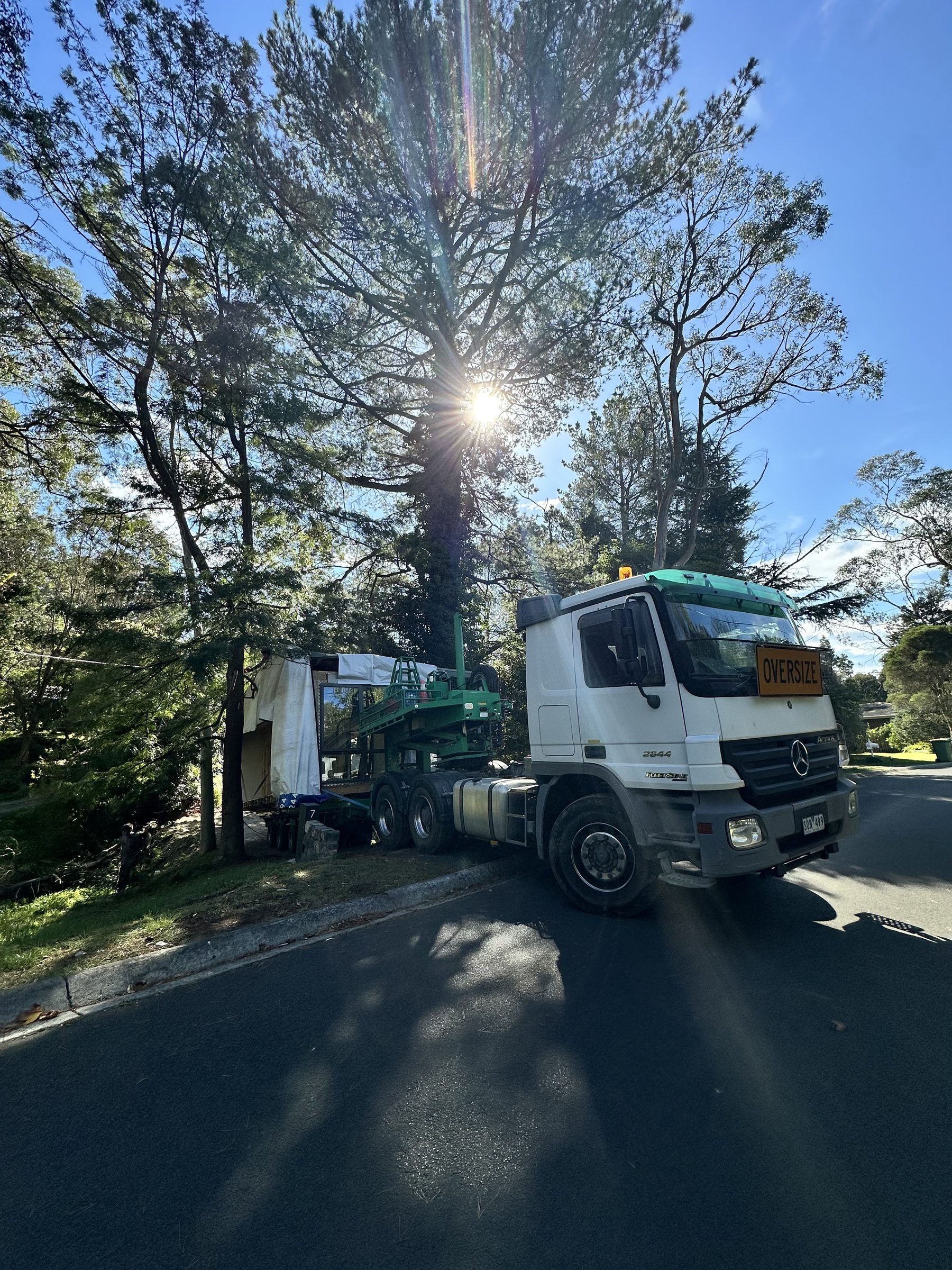 Oversize load truck moving a house through a tight, tree-lined access road